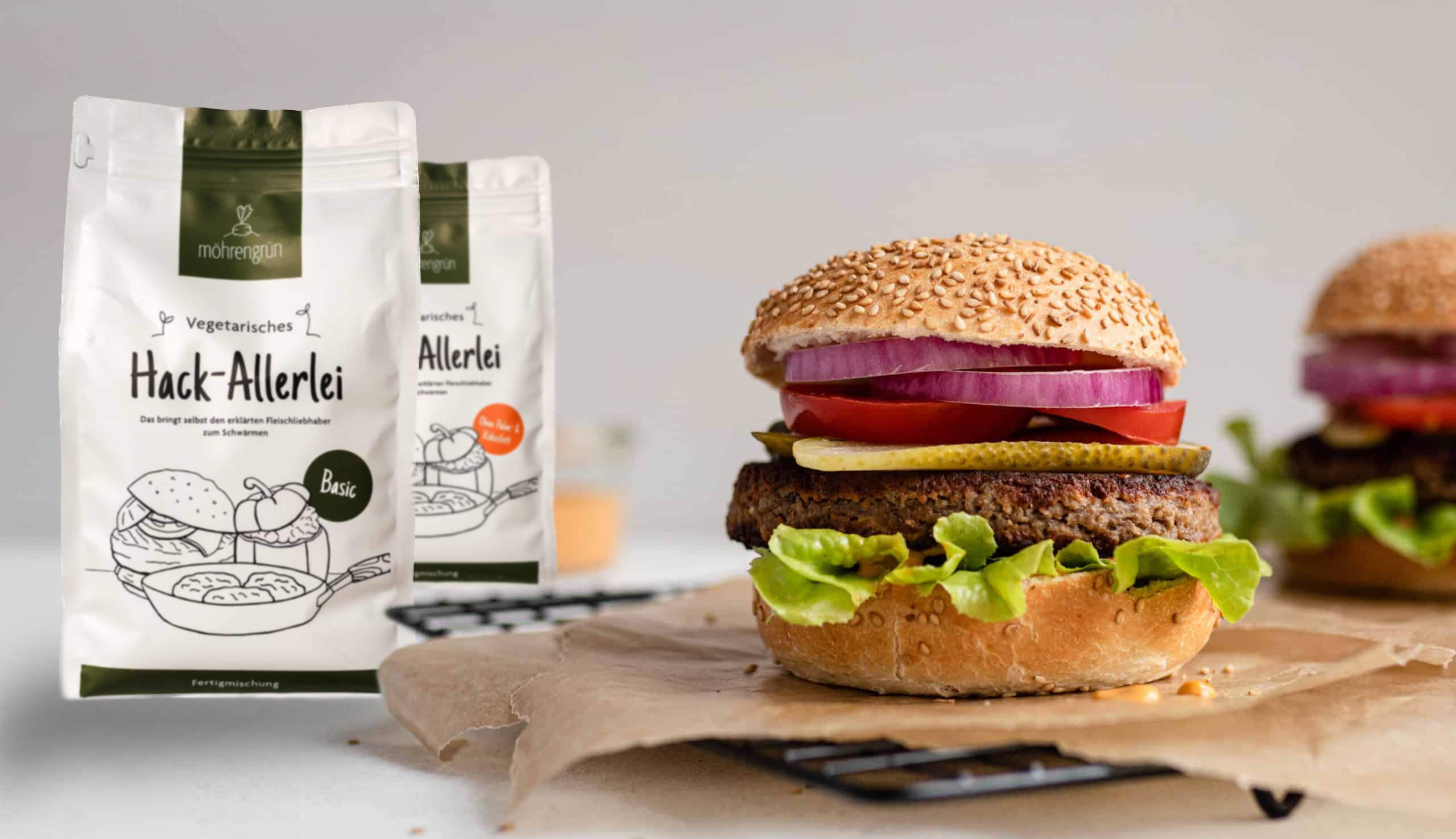 Ein vegetarischer Burger mit Sesambrötchen, Salat, Tomate und Patty wird prominent neben einer Verpackung mit der Aufschrift hack-allerlei der Marke möhrengrün präsentiert.